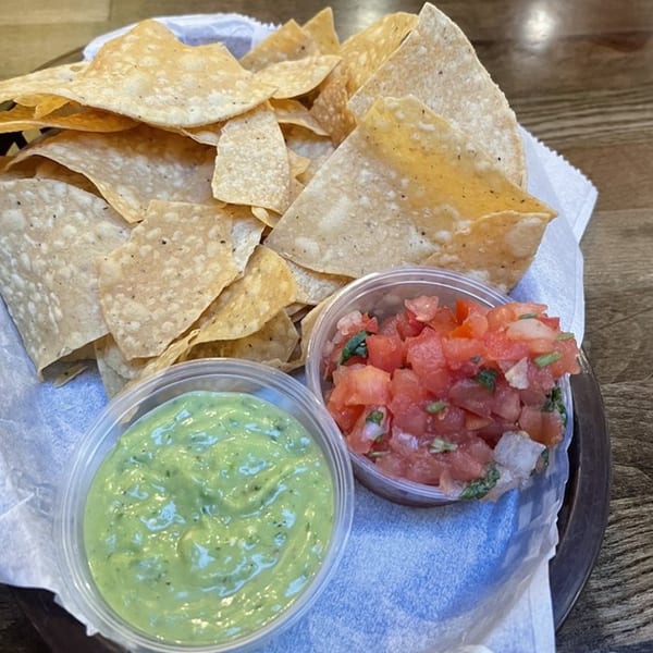 A basket of La Corneta Taqueria's tortilla chips with sides of guacamole and pico de gallo.