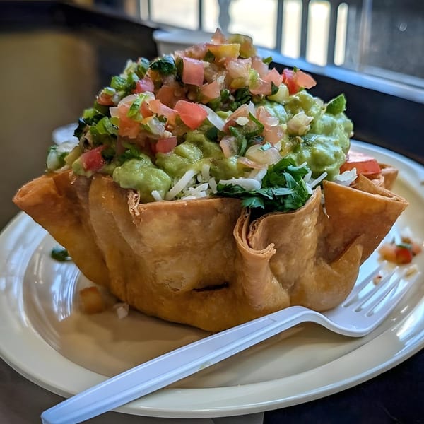 A taco salad in a crispy fried tortilla bowl, topped with guacamole, pico de gallo, and cheese.