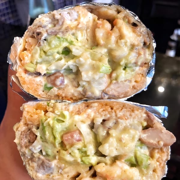 A La Corneta Taqueria burrito, cut in half, revealing a creamy filling with meat and green vegetables.