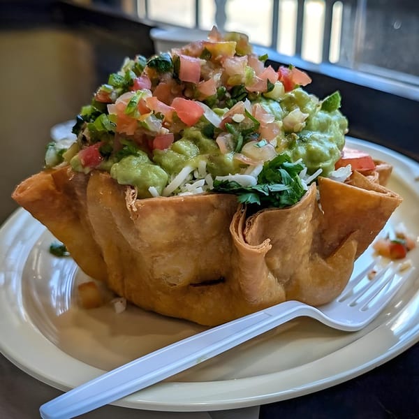 A large taco salad in a crispy fried tortilla bowl, topped with guacamole, pico de gallo, and cheese.