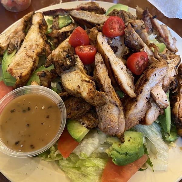 Grilled chicken salad with lettuce, avocado, tomatoes, and a side of dressing from La Corneta Taqueria.