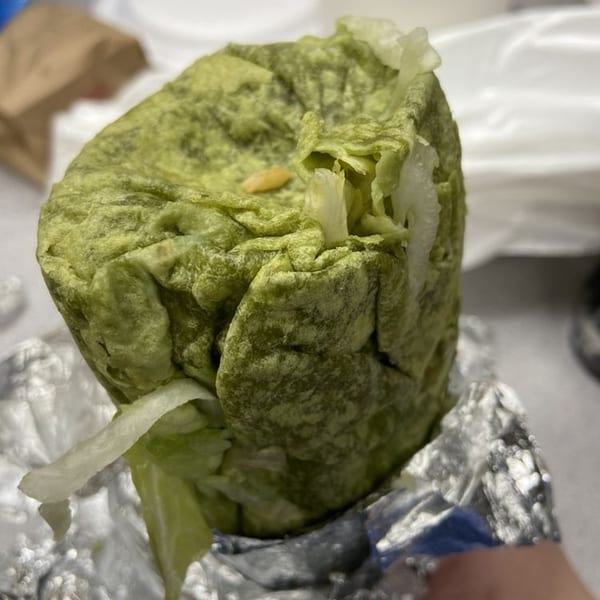 A La Corneta Taqueria burrito wrapped in green tortilla and foil, with lettuce peeking out.