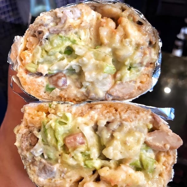 A La Corneta Taqueria burrito, cut in half, revealing a creamy filling of meat, rice, and guacamole.