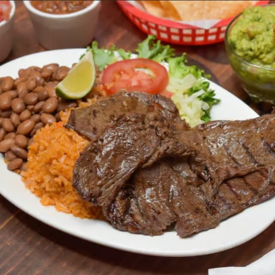 La Corneta Taqueria's carne asada plate with rice, beans, lettuce, tomato, and a lime wedge.