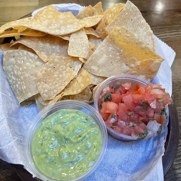 A basket of tortilla chips with small containers of green avocado salsa and red tomato salsa.