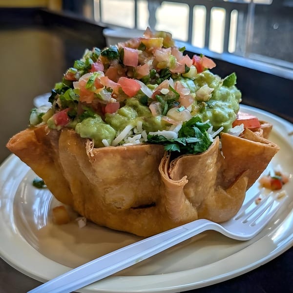 A taco salad in a crispy tortilla bowl, topped with guacamole, pico de gallo, and cheese.