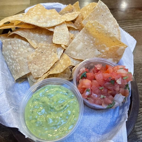 A basket of La Corneta Taqueria tortilla chips with sides of guacamole and pico de gallo.