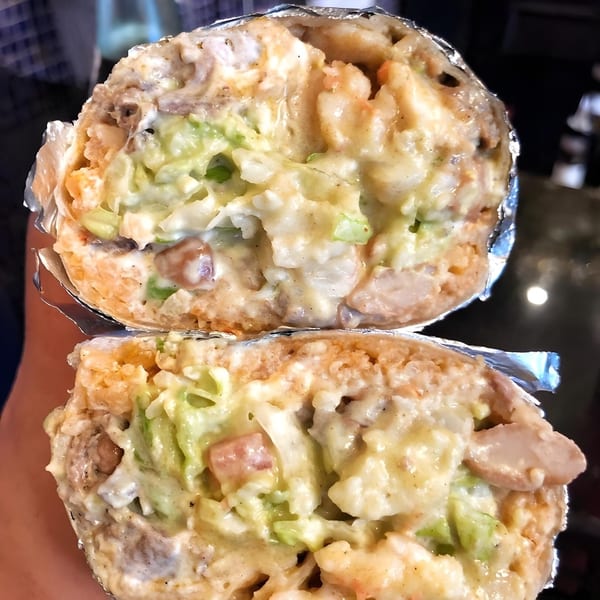 A La Corneta Taqueria burrito, cut in half, revealing a creamy filling of meat, rice, and lettuce.