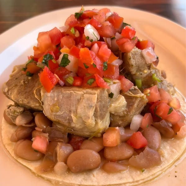La Corneta Taqueria's carnitas taco with pinto beans and fresh pico de gallo on a white plate.